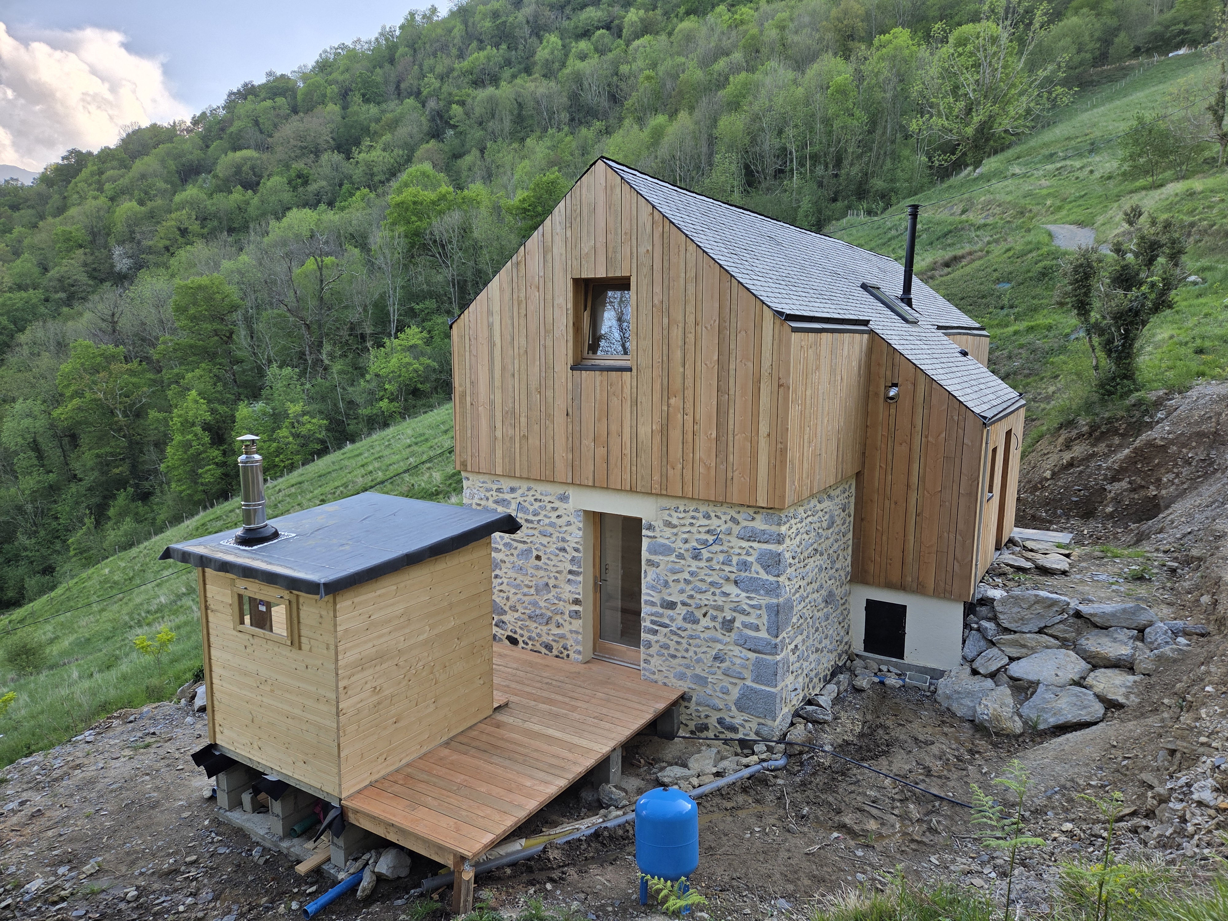 Façade de la grange en pierre et bardage bois, sur les hauteurs boisées